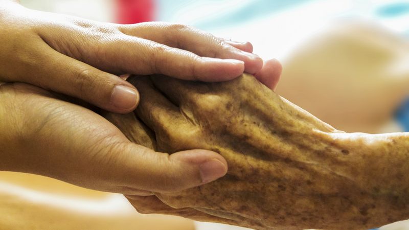 Eine Person hält die Hand eines pflegebedürftigen Menschen
