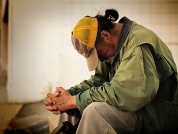 Obdachloser Mann, sitzend, mit Kappe und geneigtem Kopf