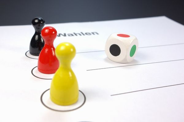 Stimmzettel, Würfel und drei farbige Spielfiguren